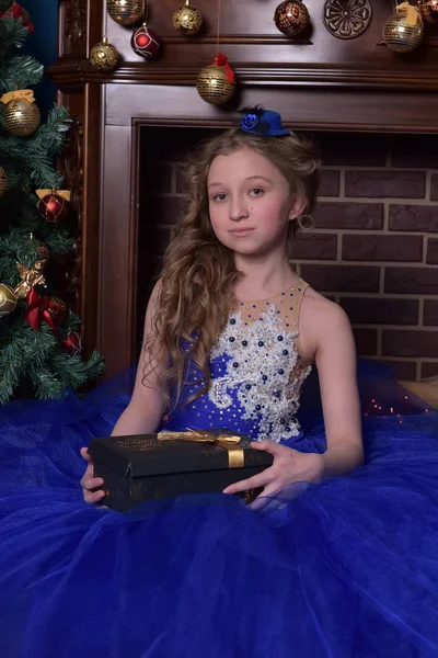 圣诞节时穿蓝色连衣裙的女孩坐在壁炉旁 — 图库照片