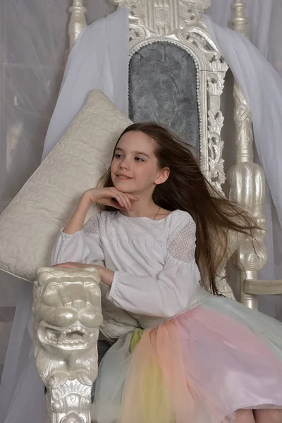Jovem de cabelos longos menina senta-se em um trono branco — Fotografia de Stock