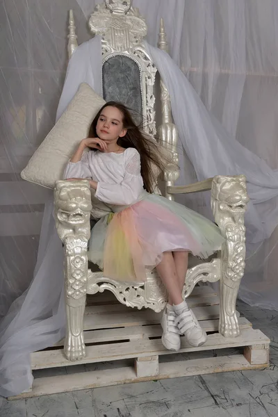 年轻的长发女孩坐在白色的宝座上 — 图库照片