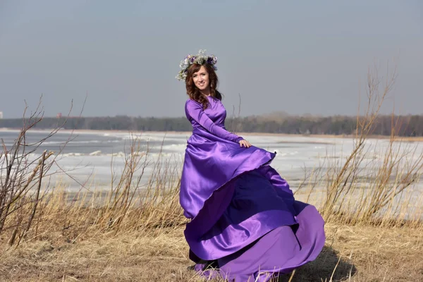 Woman lilac dress with a wreath of flowers on her head on nature in early spring