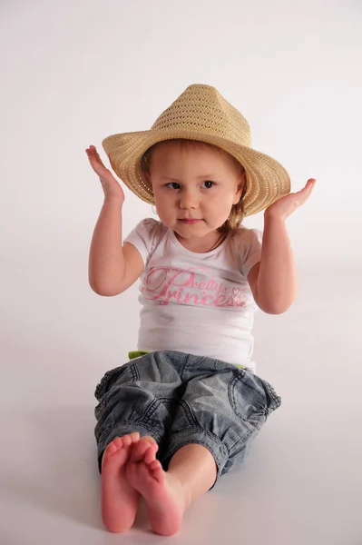 Little girl in a straw hat and jeans on a white background in th — Stock Photo, Image