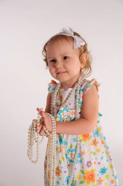 Egy kislány színes ruhában gyöngyökkel játszik. — Stock Fotó