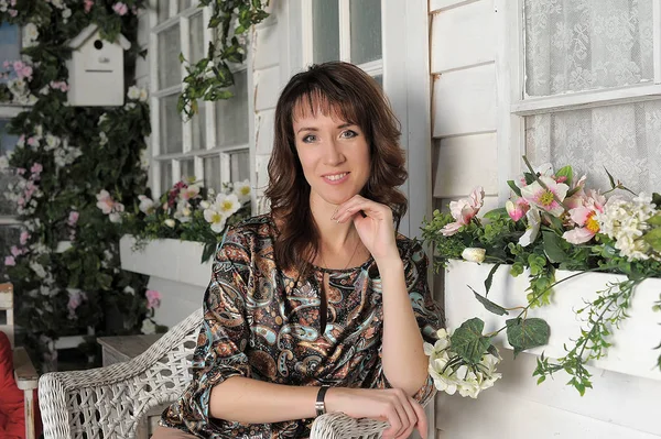 Brunette sitting on a veranda with flowers — Stockfoto