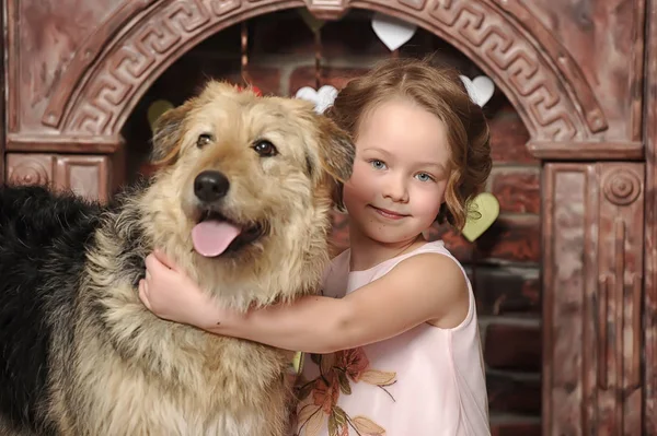 Chica en un vestido rosa con un perro mestizo junto a la chimenea — Foto de Stock