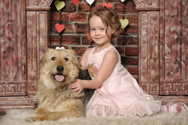 Dziewczyna w różowej sukience z psim kundlem przy kominku — Zdjęcie stockowe