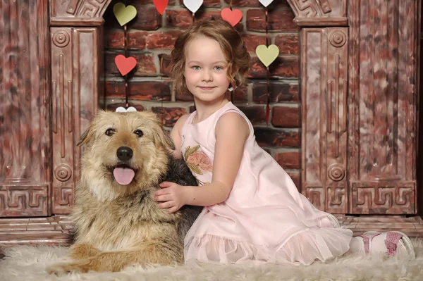 Chica en un vestido rosa con un perro mestizo junto a la chimenea — Foto de Stock