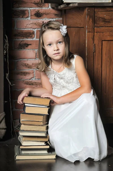 Chica en un vestido blanco con una pila de libros en el suelo en el —  Fotos de Stock