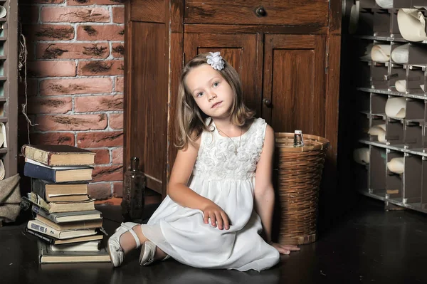 Chica en un vestido blanco con una pila de libros en el suelo en el —  Fotos de Stock
