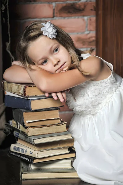 Menina em um vestido branco com uma pilha de livros no chão no — Fotografia de Stock