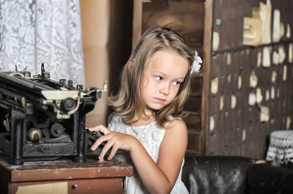 Süßes Mädchen in einem weißen Kleid mit einer alten Schreibmaschine — Stockfoto