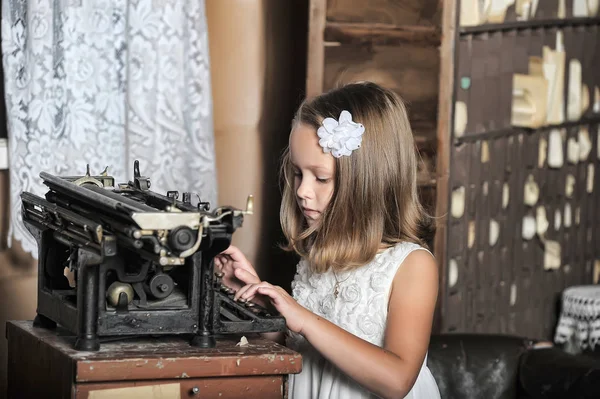 Menina bonito em um vestido branco com uma máquina de escrever vintage — Fotografia de Stock