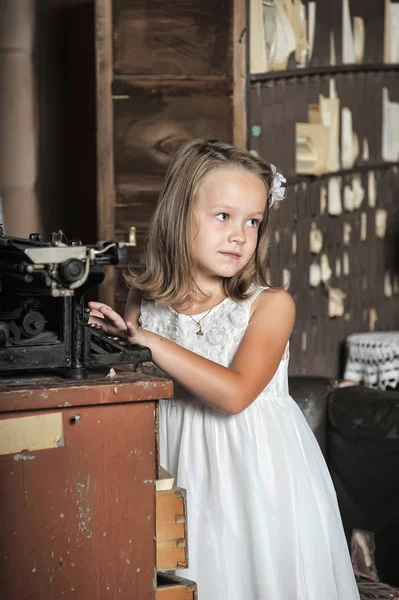 Cute girl in a white dress with a vintage typewriter — Stock Photo, Image