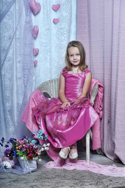 Roztomilá dívka v růžových šatech sedí na židli — Stock fotografie