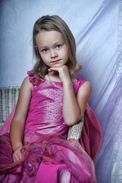 Menina bonito em um vestido rosa senta-se em uma cadeira — Fotografia de Stock