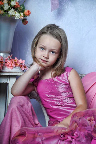 Schattig meisje in een roze jurk zit op een stoel — Stockfoto