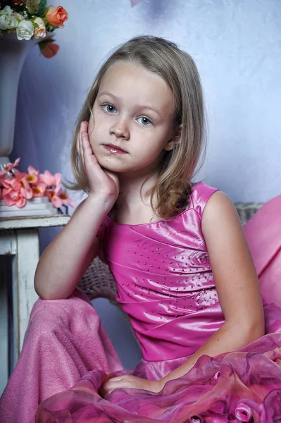 Menina bonito em um vestido rosa senta-se em uma cadeira — Fotografia de Stock