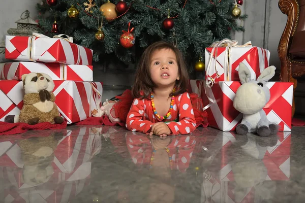 Το κοριτσάκι με το φόρεμα κοντά στο χριστουγεννιάτικο δέντρο κείτεται στο πάτωμα. — Φωτογραφία Αρχείου