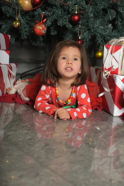 在圣诞树旁穿着连衣裙的小女孩躺在地板上 — 图库照片