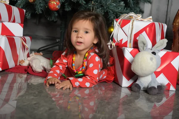 Klein meisje in een jurk bij de kerstboom ligt op de vloer — Stockfoto