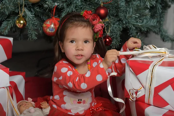 Bambina in abito rosso vicino all'albero di Natale tra i regali — Foto Stock