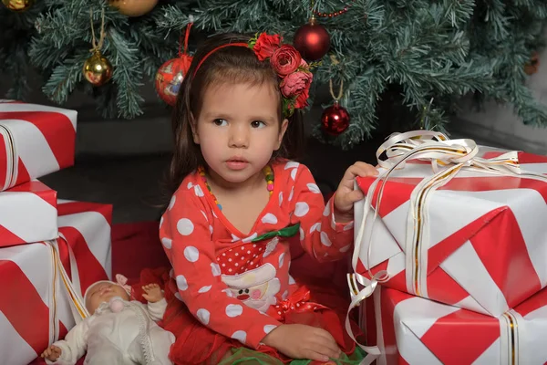 Meisje in een rode jurk in de buurt van de kerstboom tussen geschenken — Stockfoto