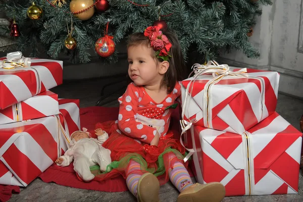 Маленькая девочка в красном платье рядом с елкой среди подарков — стоковое фото
