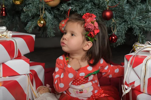 Маленькая девочка в красном платье рядом с елкой среди подарков — стоковое фото