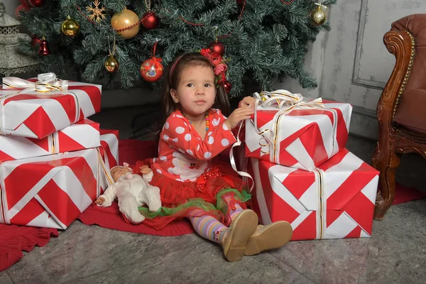 Noel ağacının yanında kırmızı elbiseli küçük kız hediyelerin arasında. — Stok fotoğraf