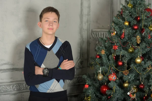 Adolescente ragazzo in un maglione si trova accanto a un albero di Natale — Foto Stock