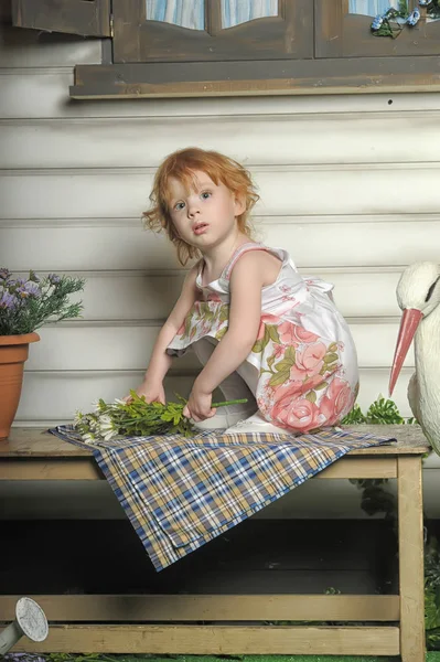 Klein roodharig meisje in een witte jurk met een boeket bloemen — Stockfoto