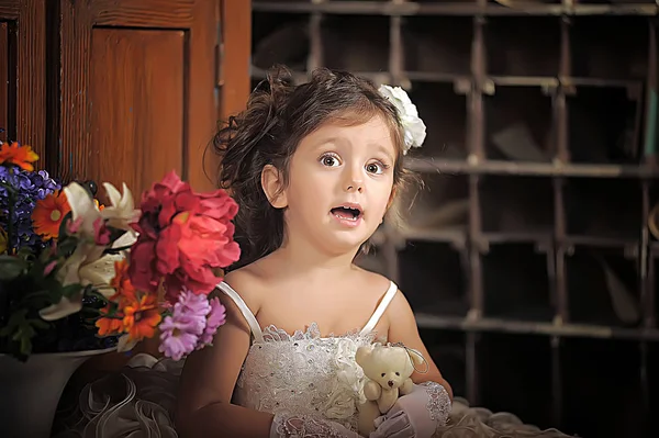 Een mooi meisje, een kind in een mooie jurk en een vaas bloemen — Stockfoto