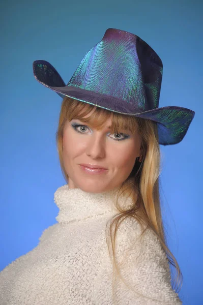 Long-haired blonde in a studio on a blue background in a hat — Stok fotoğraf