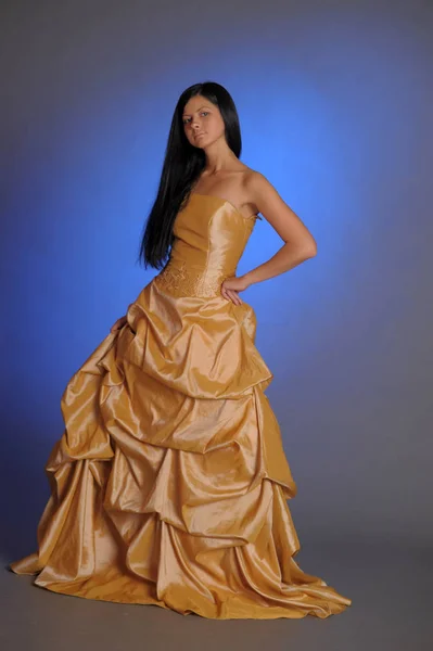 Brunette girl in a long golden dress in the studio — 스톡 사진