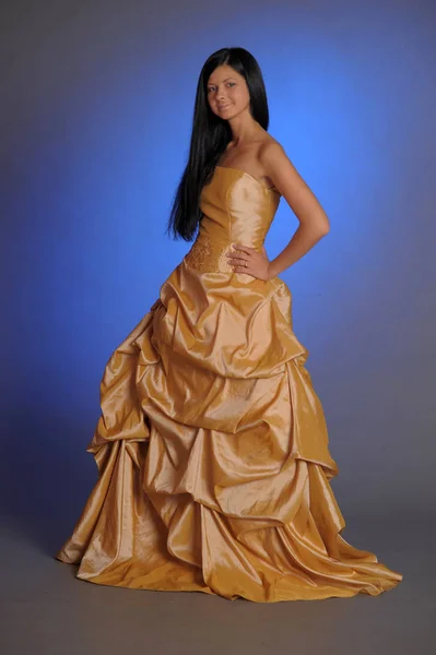 Брюнетка в длинном золотом платье в студии — стоковое фото