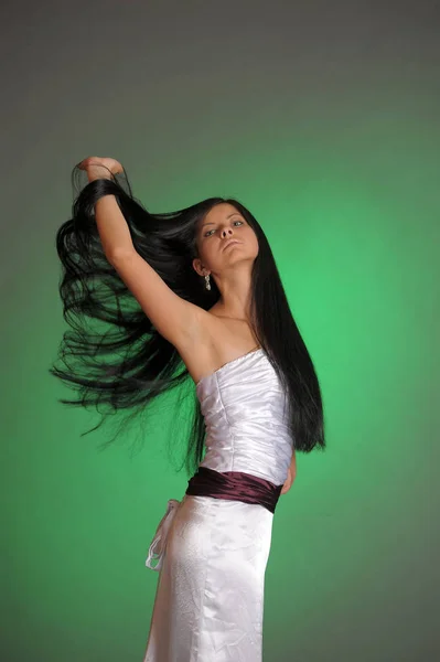 Brunette girl in a long white dress in the studio on a green bac — Stock Photo, Image