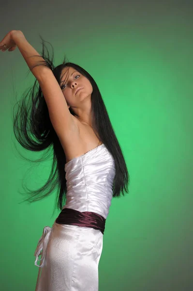 Brünettes Mädchen in einem langen weißen Kleid im Studio auf einem grünen Bac — Stockfoto
