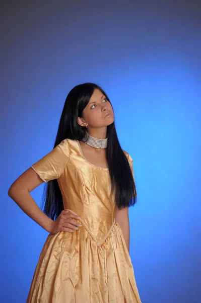 Brunette girl in a long golden dress in the studio — Stock Photo, Image