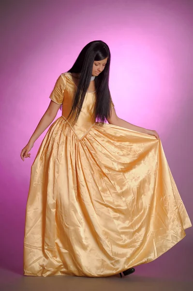 Brunette girl in a long golden dress in the studio — Stock Photo, Image