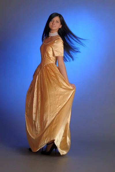 Brünettes Mädchen in einem langen goldenen Kleid im Studio — Stockfoto