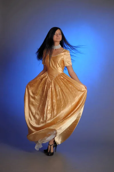 Brünettes Mädchen in einem langen goldenen Kleid im Studio — Stockfoto