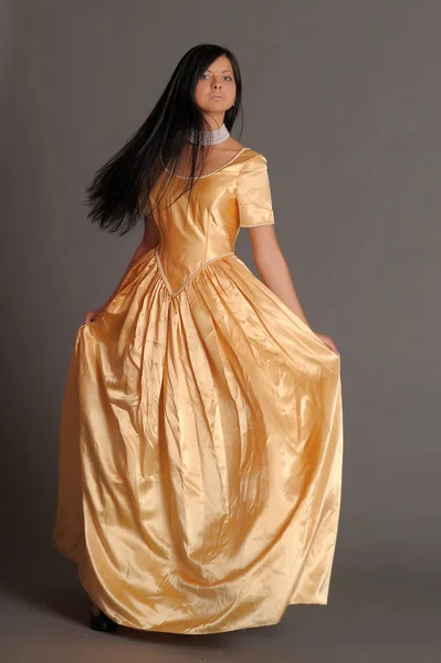 Brunett flicka i en lång gyllene klänning i studion — Stockfoto