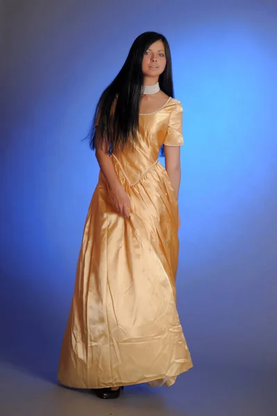 Brunette girl in a long golden dress in the studio — 스톡 사진