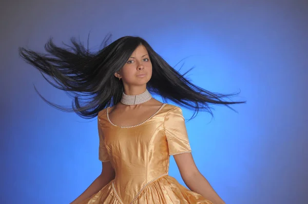 Brünettes Mädchen in einem langen goldenen Kleid im Studio — Stockfoto