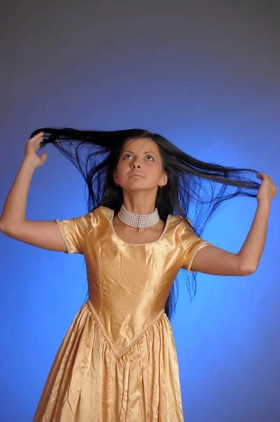 Брюнетка дівчина в довгій золотій сукні в студії — стокове фото