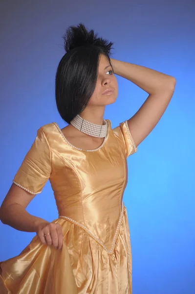 Brunette girl in a long golden dress in the studio — 스톡 사진