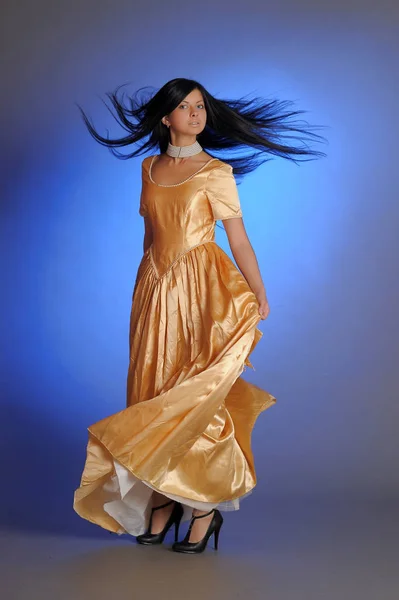 Menina morena em um vestido dourado longo no estúdio — Fotografia de Stock