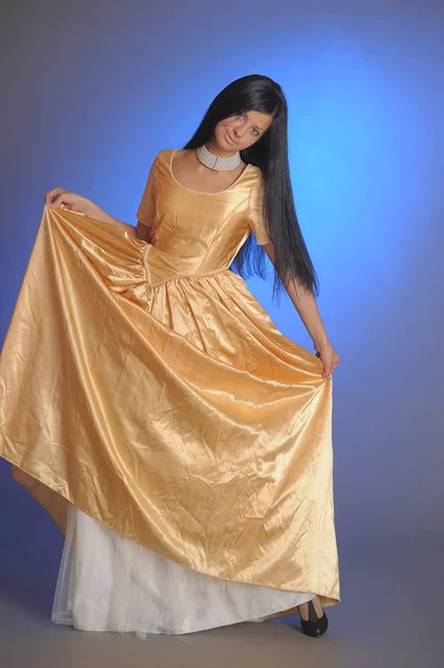 Brunette girl in a long golden dress in the studio — 스톡 사진