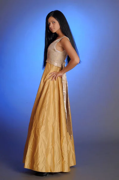 Brünettes Mädchen in einem langen goldenen Kleid im Studio — Stockfoto
