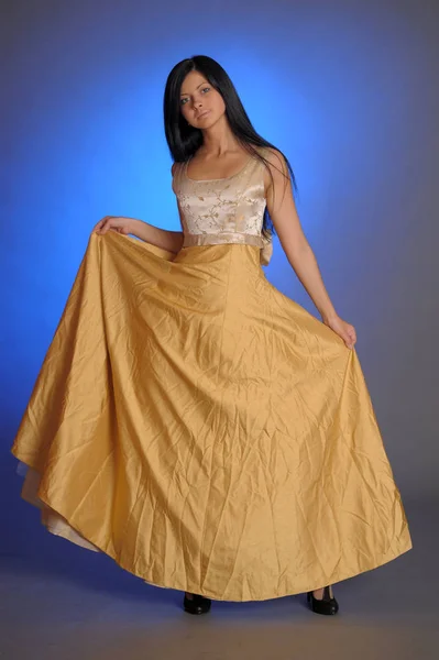 Brünettes Mädchen in einem langen goldenen Kleid im Studio — Stockfoto
