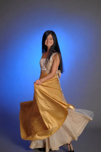 Brunette girl in a long golden dress in the studio — 스톡 사진